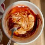 White bowl with a spoon in it mixing mayo and barbecue sauce together.