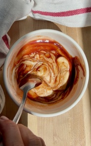 White bowl with a spoon in it mixing mayo and barbecue sauce together.