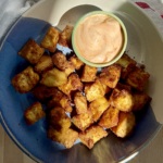 Golden brown tofu in a blue and white bowl on a cutting board with a sauce on the side