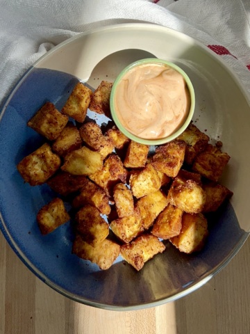 Golden brown tofu in a blue and white bowl on a cutting board with a sauce on the side