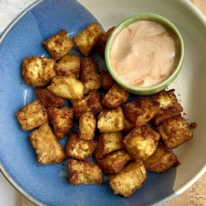 Golden brown tofu in a blue and white bowl on a cutting board with a sauce on the side