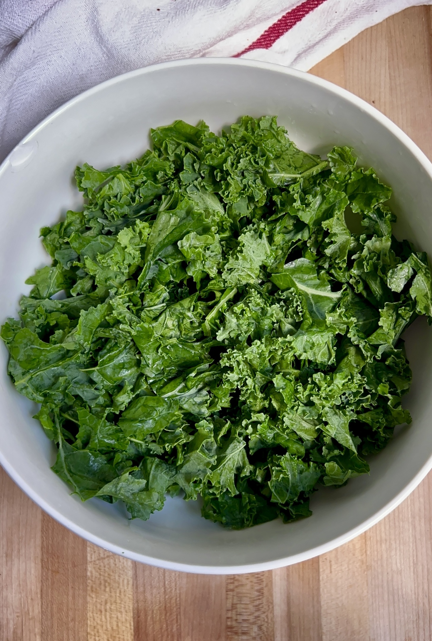 Bowl of shredded kale on a cutting board with a white cloth to the side.