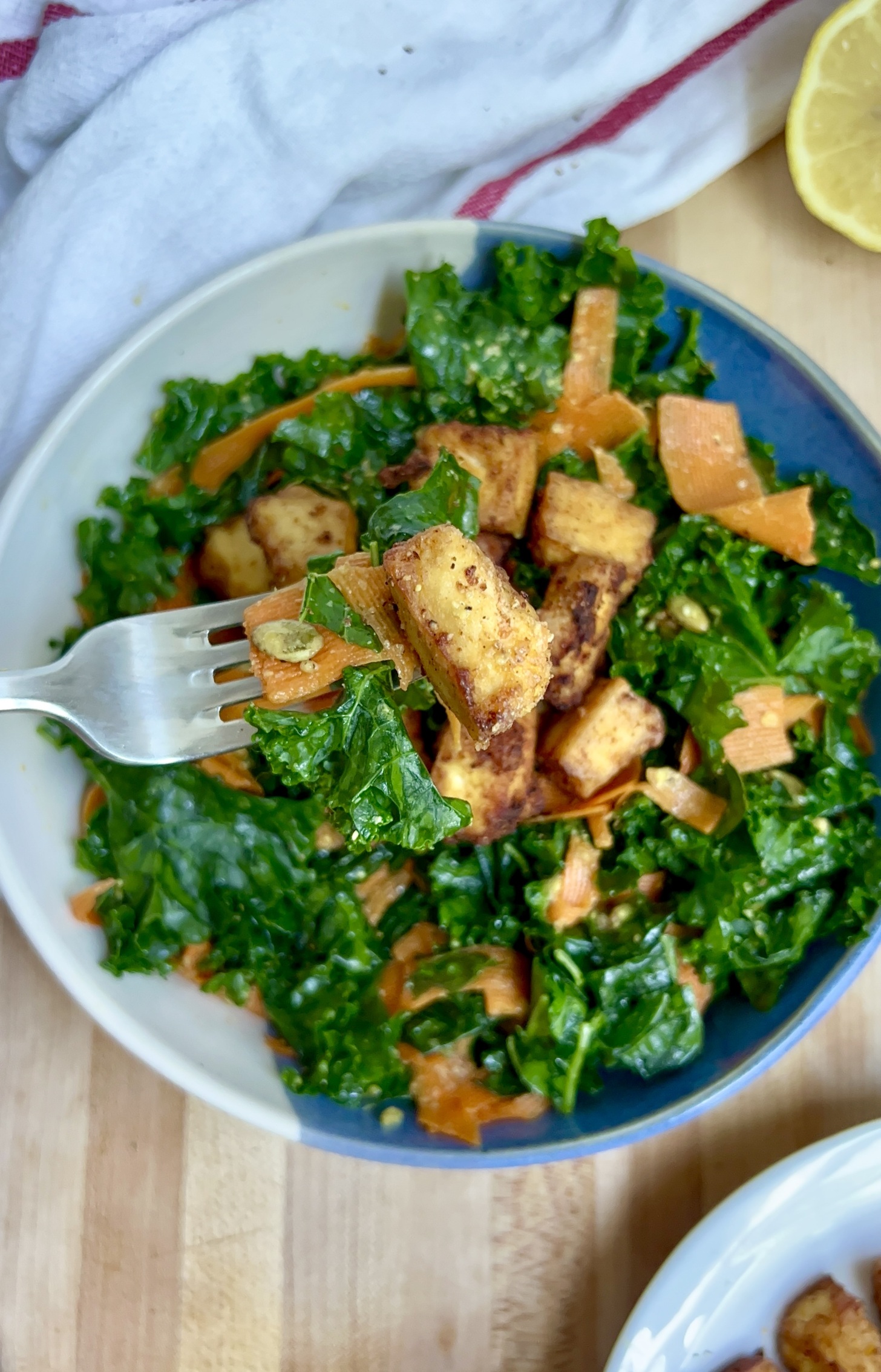 Blue and white bowl with salad and golden brown tofu inside with a fork piercing a piece of tofu