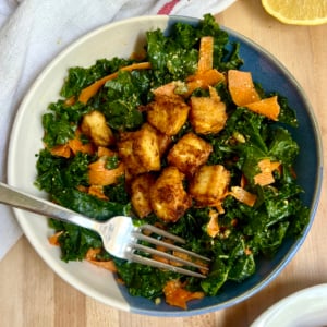 Blue and white bowl with salad and golden brown tofu inside with a lemon off to the side and fork in the bowl