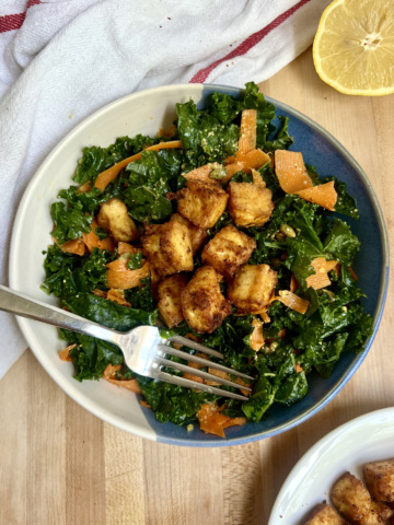 Blue and white bowl with salad and golden brown tofu inside with a lemon off to the side and fork in the bowl