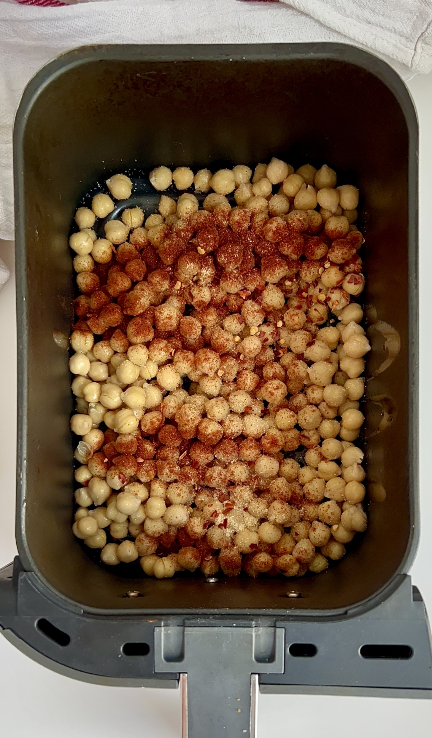 Air fryer with chickpeas inside sprinkled with smoked paprika