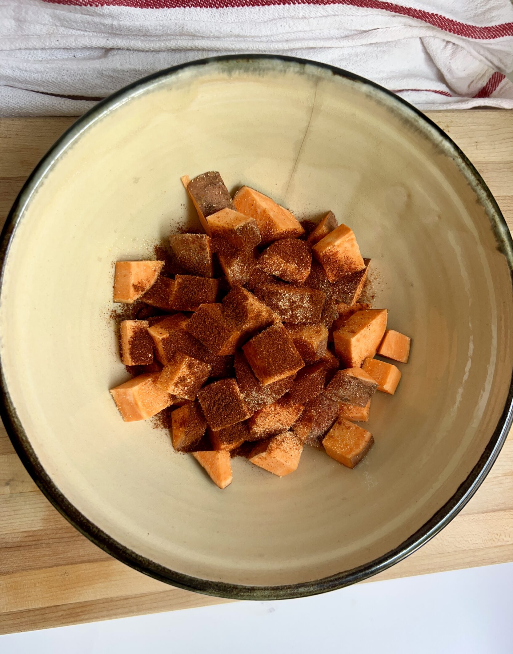 Large bowl with cubed sweet potato in it with spices on top.
