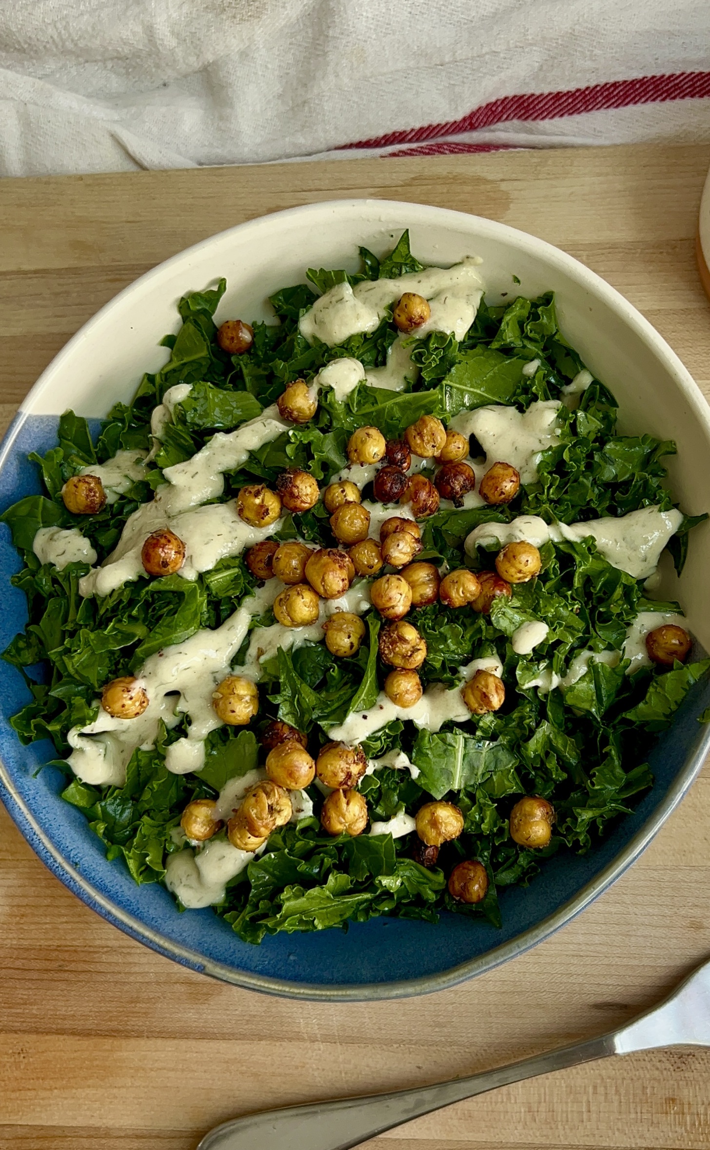 White and blue bowl with massaged kale and tahini dressing and roasted chickpeas on top.