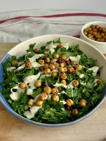 White and blue bowl with massaged kale and tahini dressing and roasted chickpeas on top and a bowl of roasted chickpeas to the side.