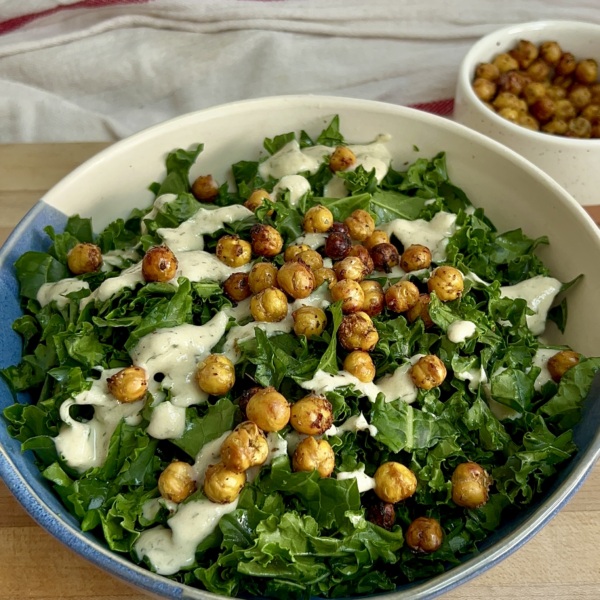 White and blue bowl with massaged kale and tahini dressing and roasted chickpeas on top and a bowl of roasted chickpeas to the side.