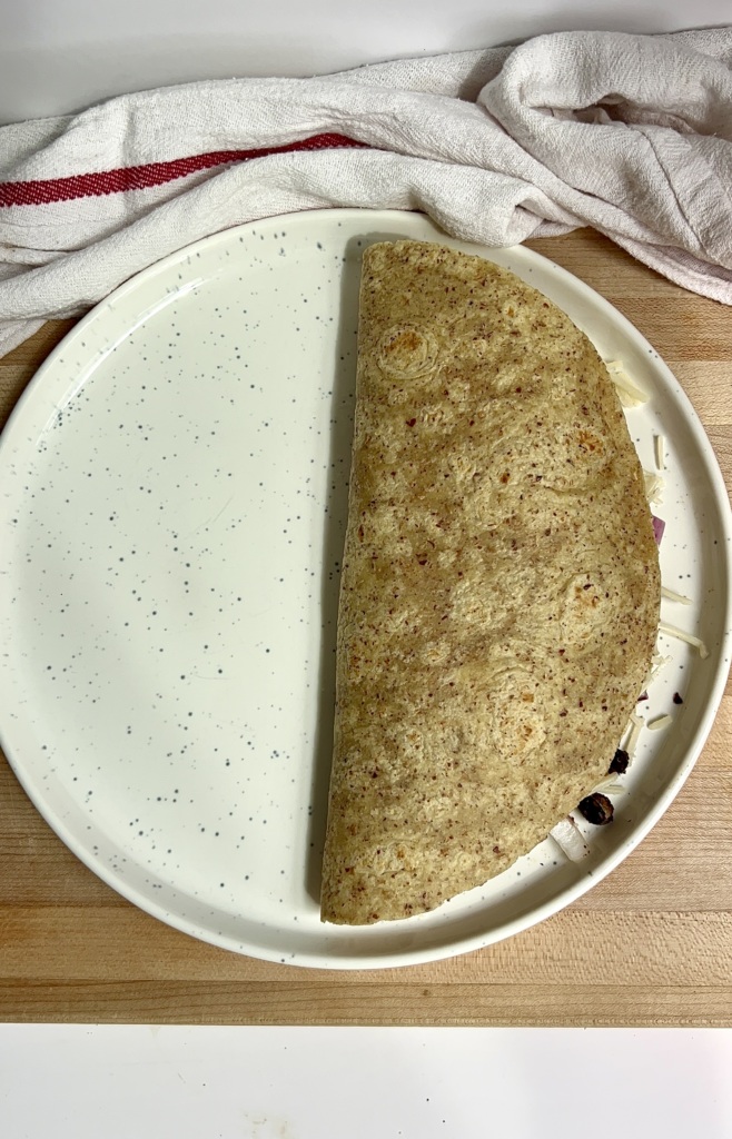 White plate on parchment paper with a folded over quesadilla on it.
