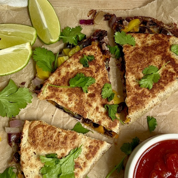 Cooked quesadilla sliced into 3 on parchment paper with cilantro on top, lime to the side and salsa next to it.