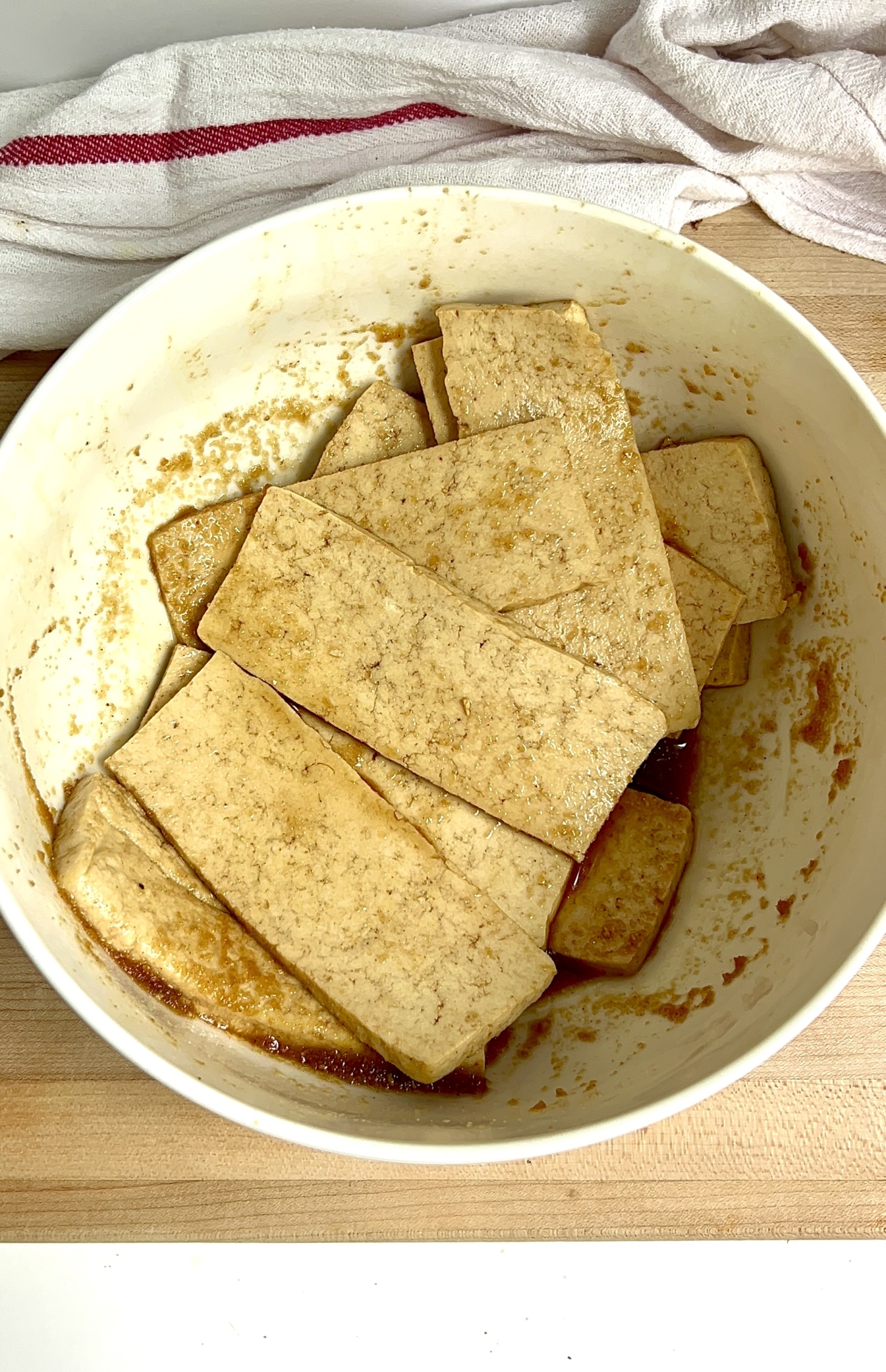 White bowl with sliced tofu and marinade on top.