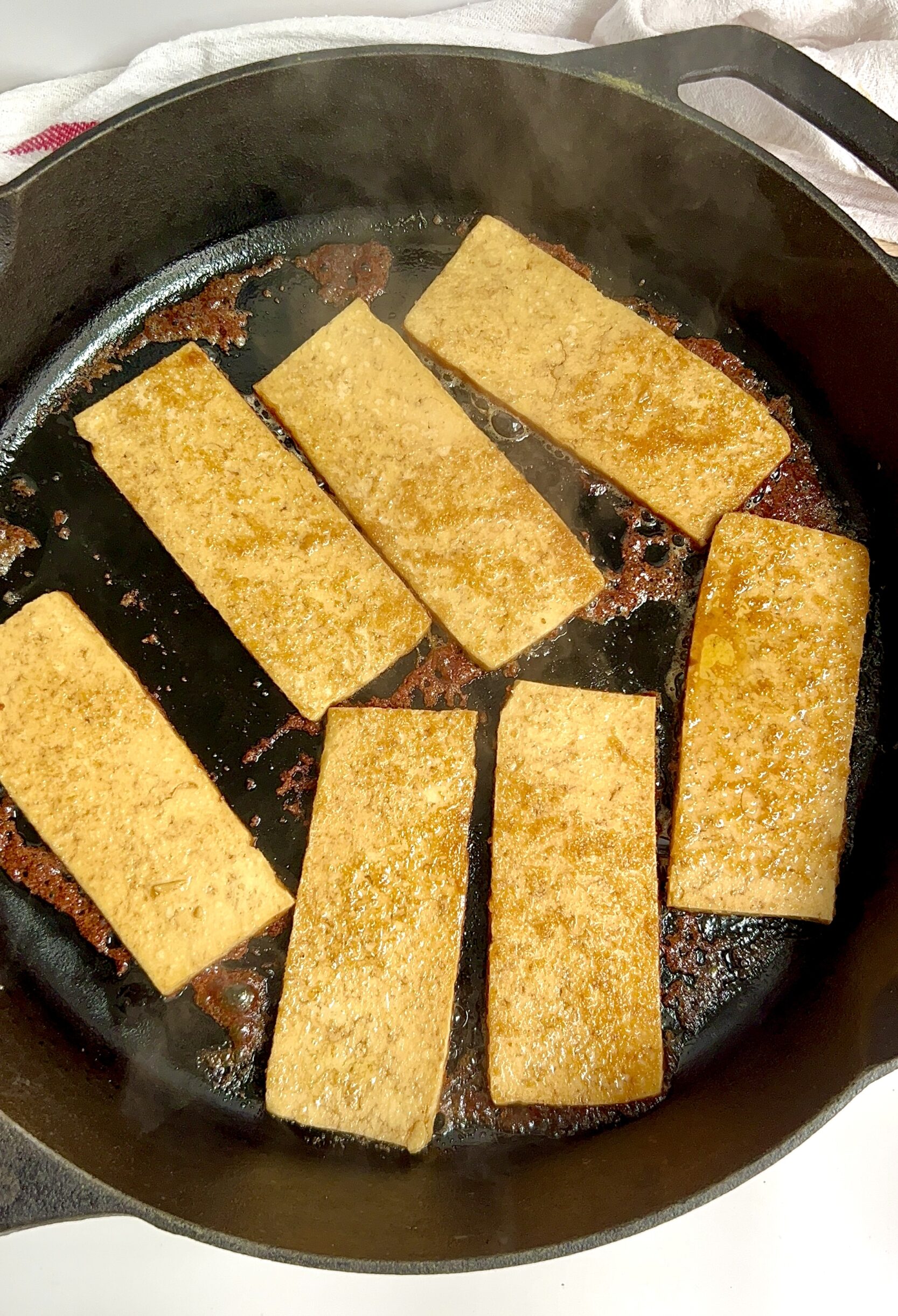 Cast iron pan with golden brown marinated sliced tofu cooking.