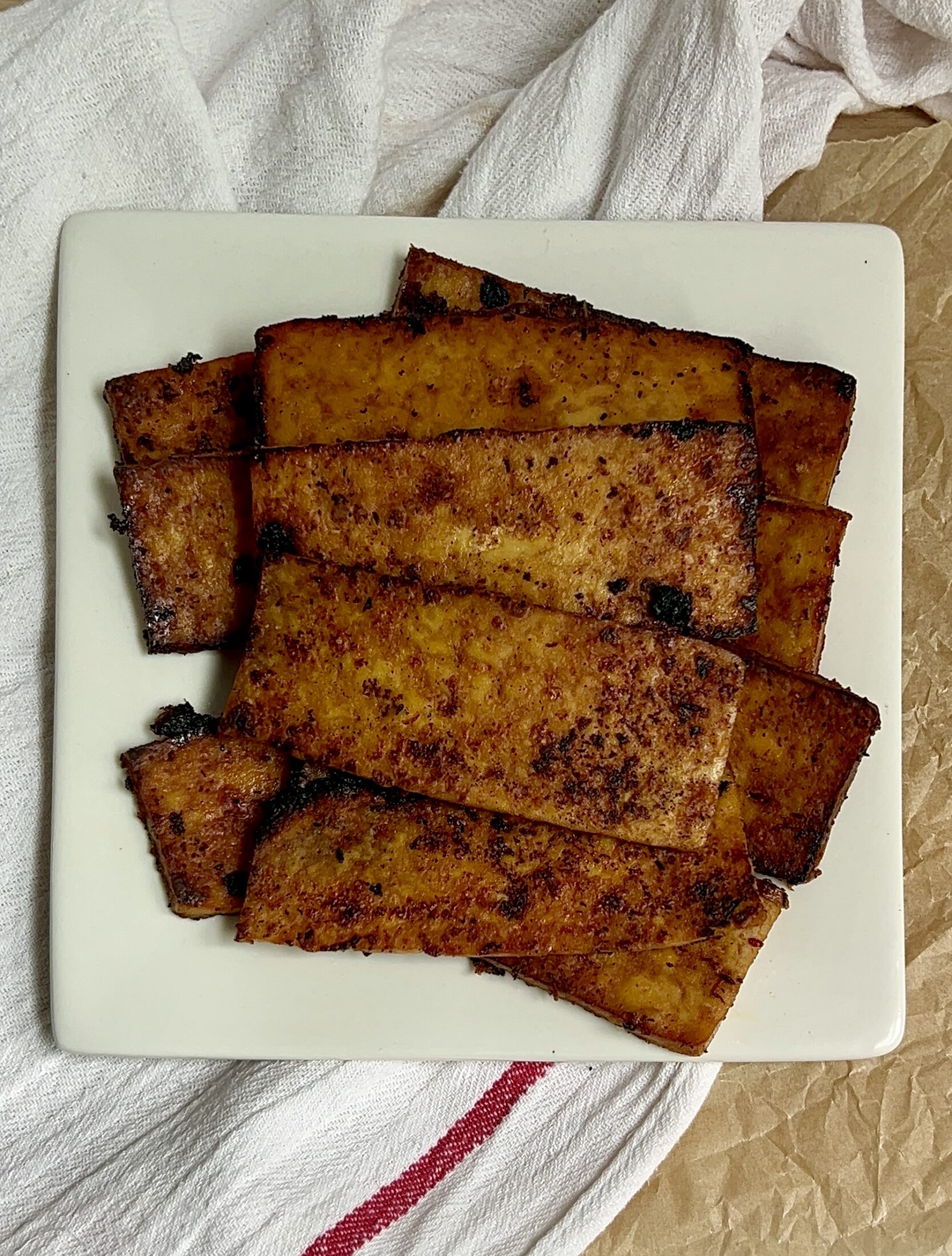 Plate of strips of tofu with a marinade on them that are golden brown.
