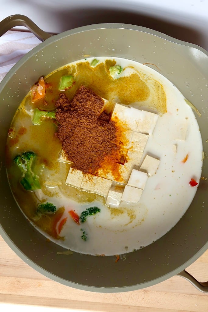 Large pot with diced tofu, coconut milk, veggies and curry powder inside.