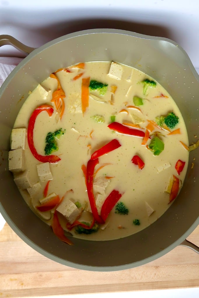 Large pot with sliced veggies, diced tofu, and coconut milk with curry powder inside.
