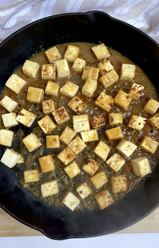 Cubed tofu in a pan with a sauce poured on top.