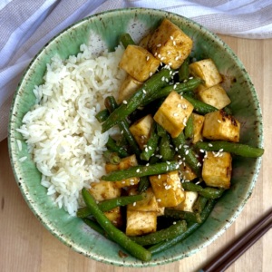 Bowl of tofu with green beans and rice on the side