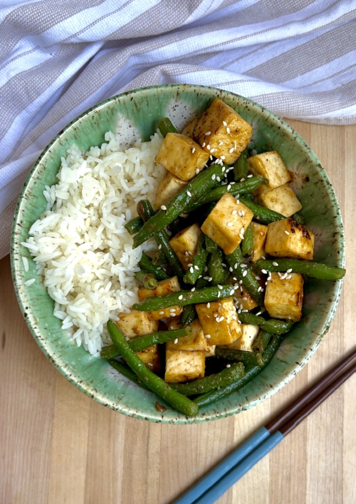 Bowl of tofu with green beans and rice on the side