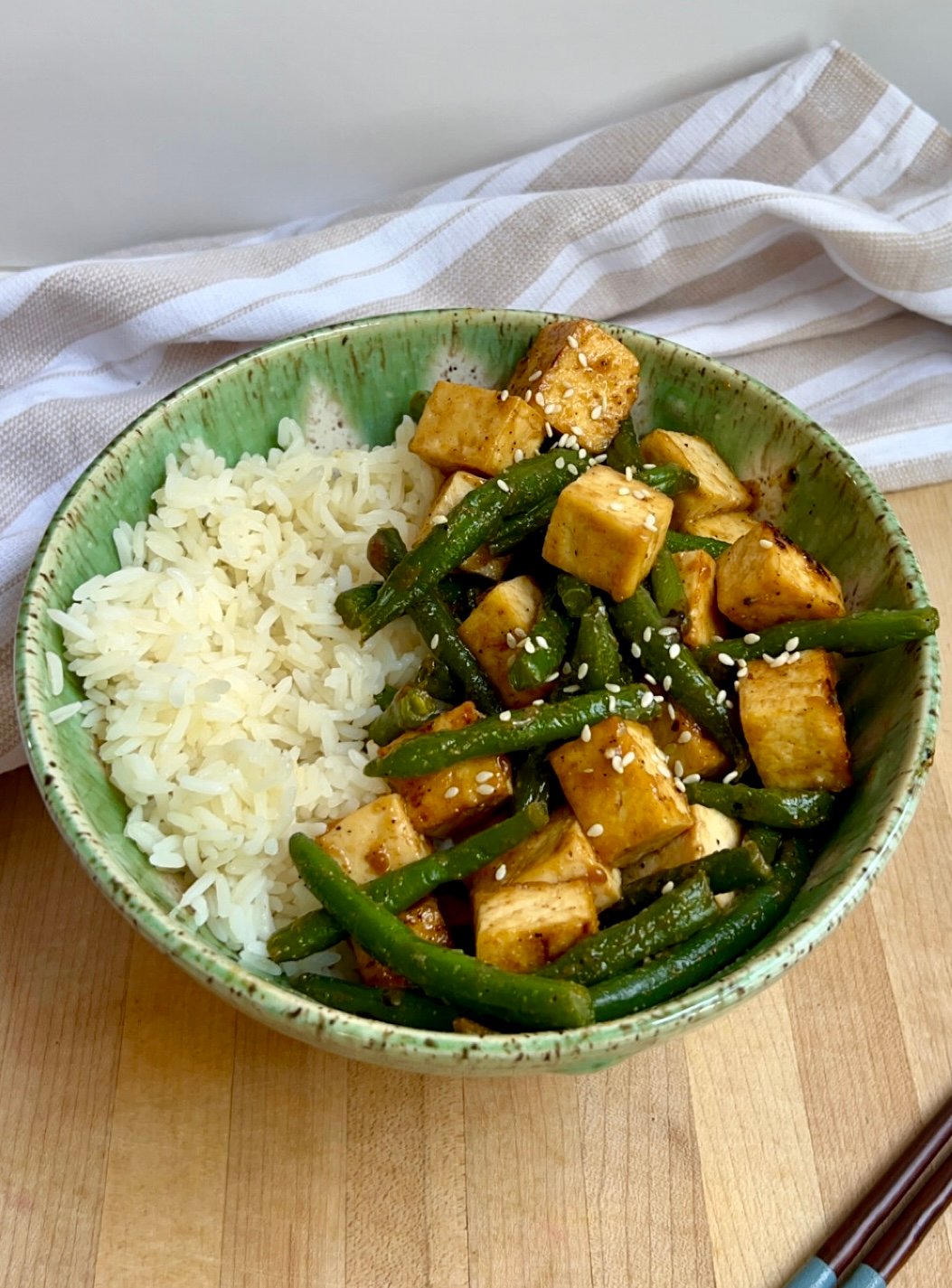 Bowl of tofu with green beans and rice on the side