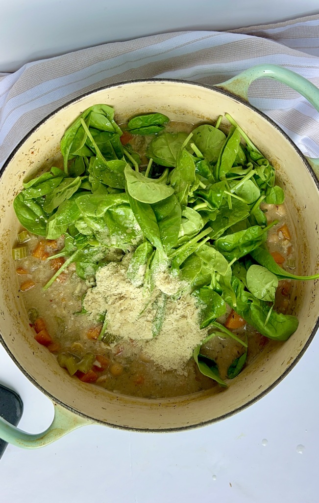 Large pot with lots of soup inside and spinach.