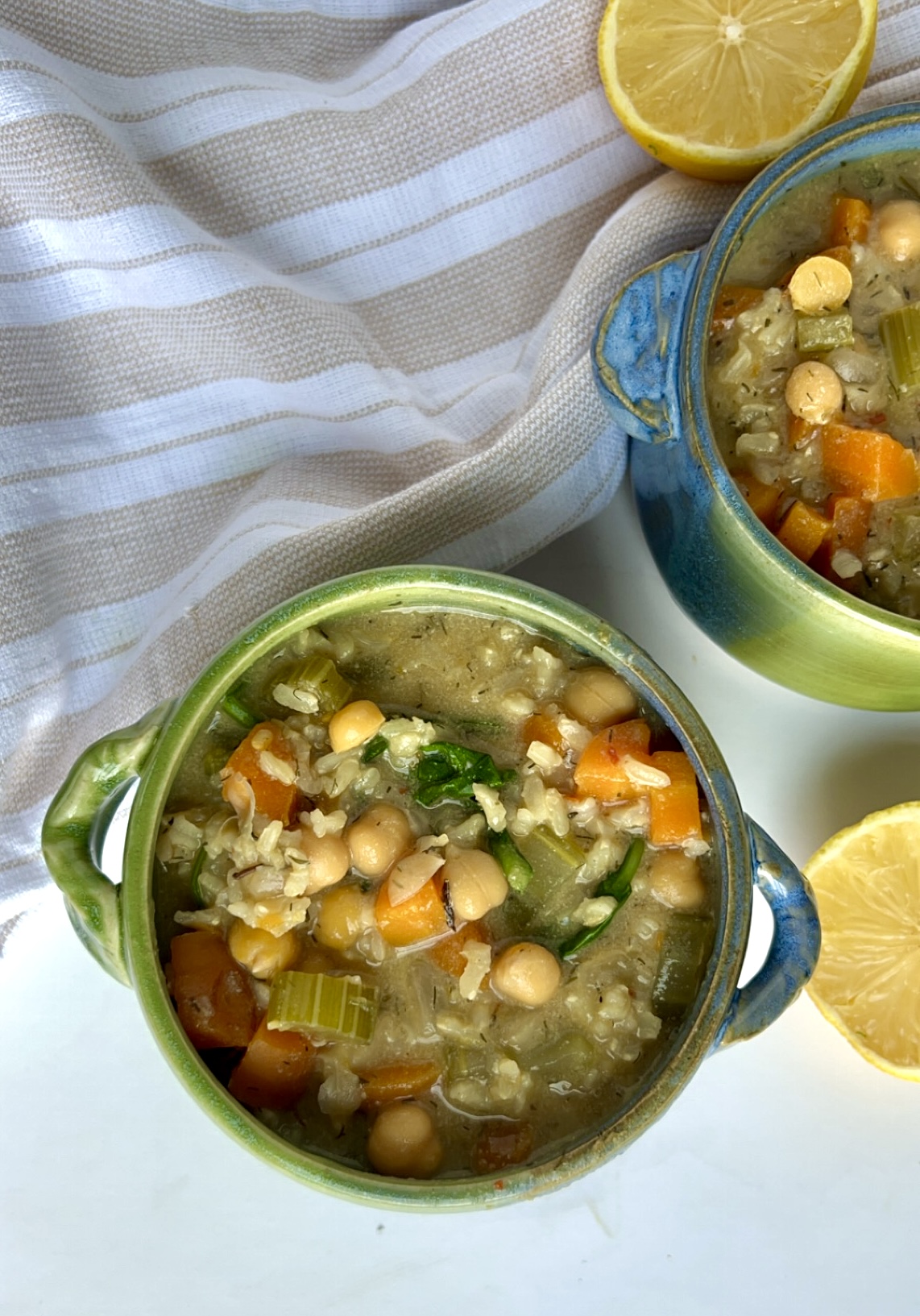 Two small blue and green soup bowls with soup inside with chickpeas, celery and rice.