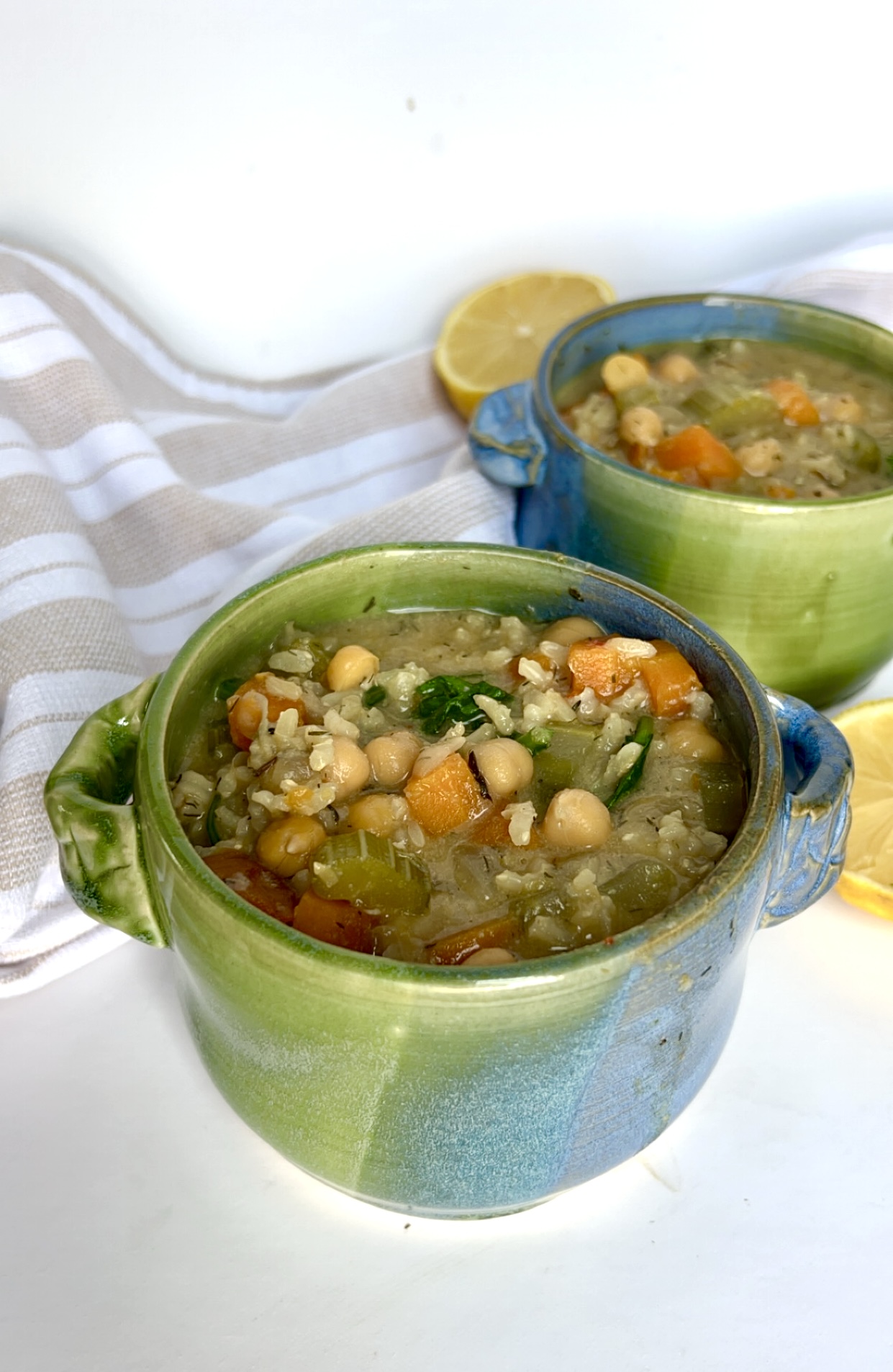 Two small blue and green soup bowls with soup inside with chickpeas, celery and rice.