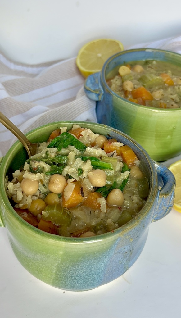 Two small blue and green soup bowls with soup inside with chickpeas, celery and rice.