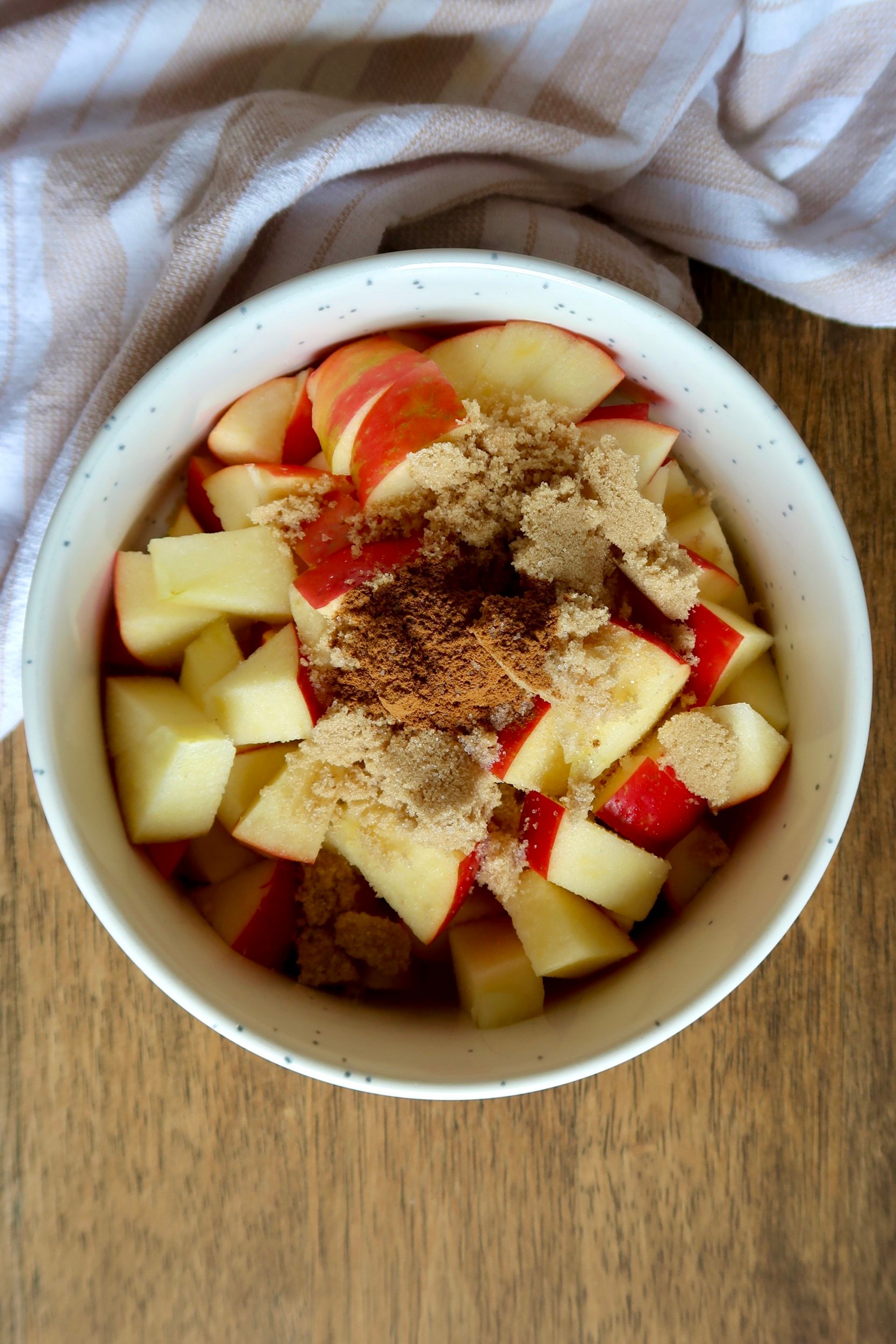 White bowl with diced apple inside as well as cinnamon and brown sugar.