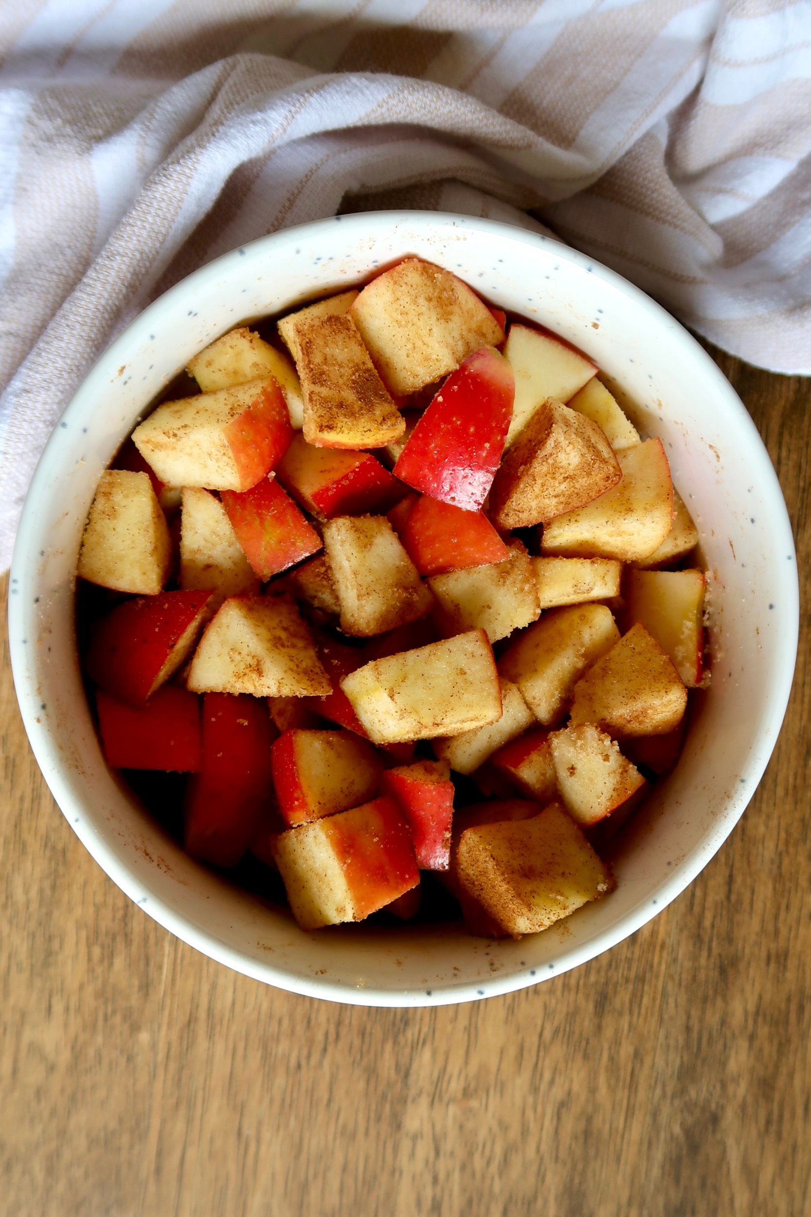 White bowl with diced apple inside covered in cinnamon