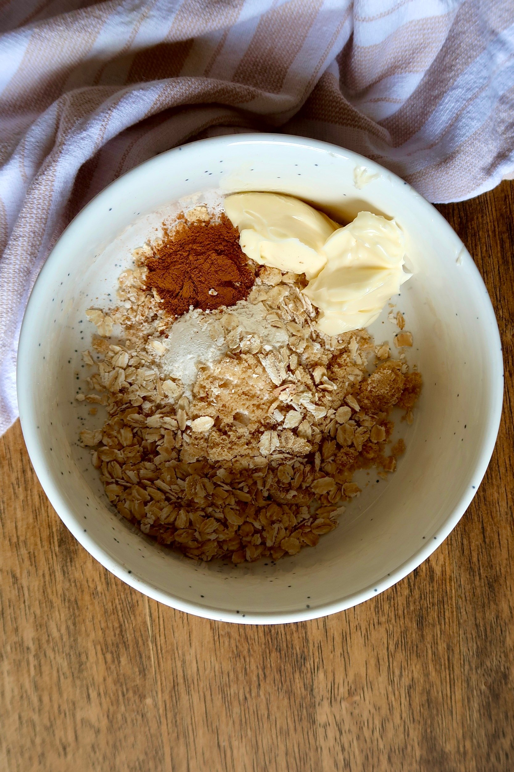 White bowl with oats, cinnamon, brown sugar and butter inside.