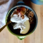 Blue and green ramekin with apple crisp inside and whipped cream with a spoon holding some.
