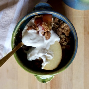 Blue and green ramekin with apple crisp inside and whipped cream with a spoon holding some.