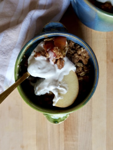 Blue and green ramekin with apple crisp inside and whipped cream with a spoon holding some.