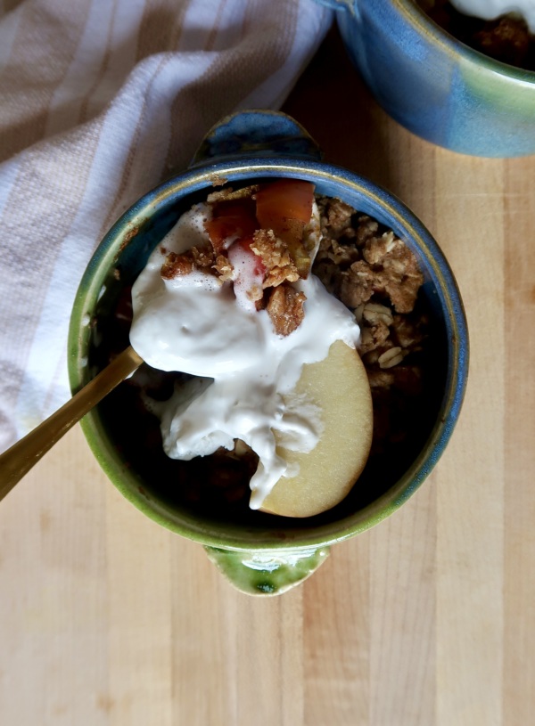 Blue and green ramekin with apple crisp inside and whipped cream with a spoon holding some.