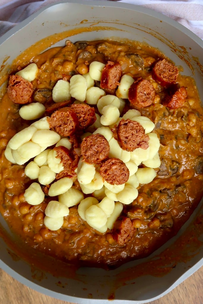 Pan with pumpkin sauce inside and uncooked gnocchi and sausage