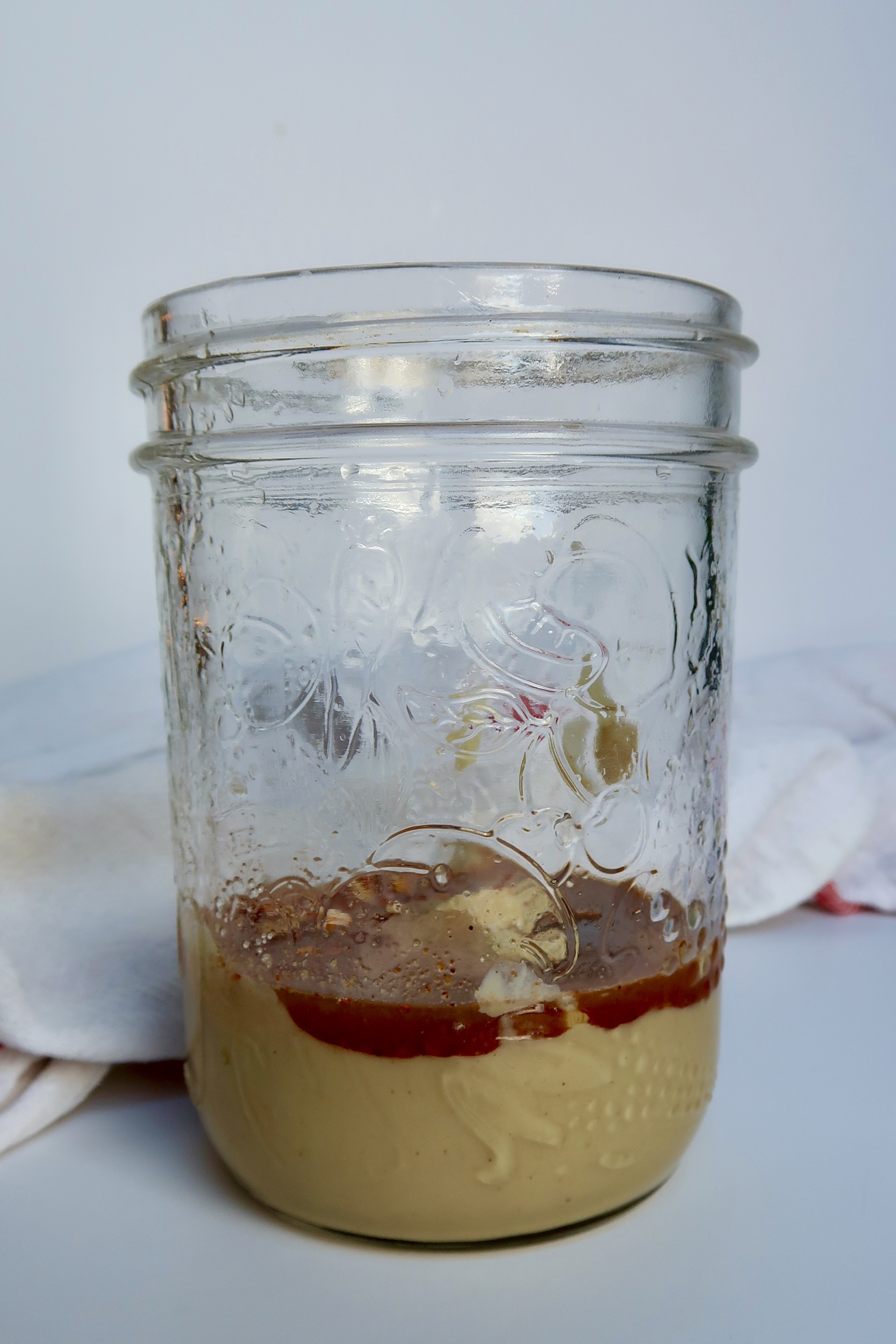 Jar in white background with tahini and chili powder inside.