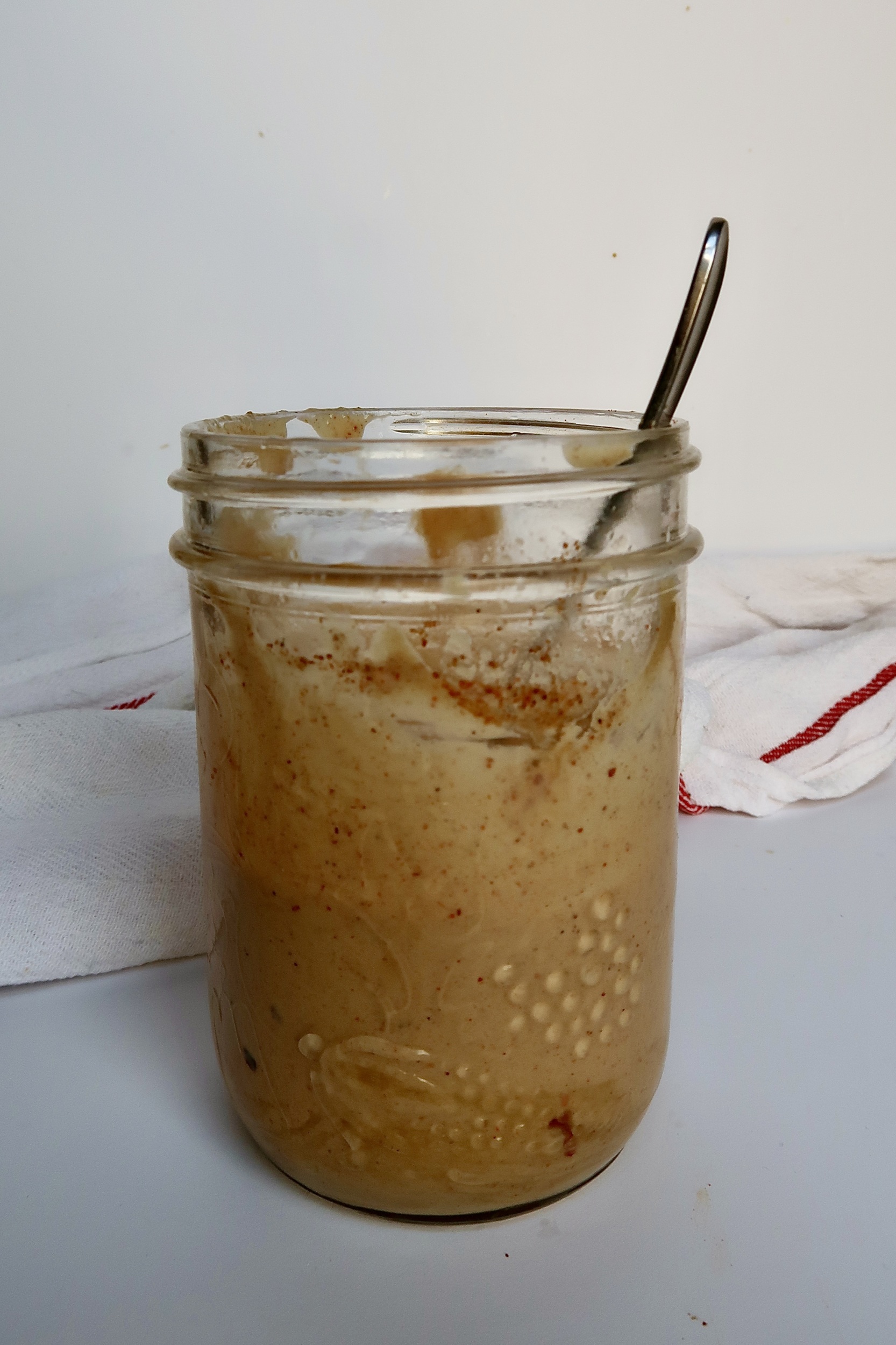 Jar ion white background with tahini dressing inside and spoon resting.