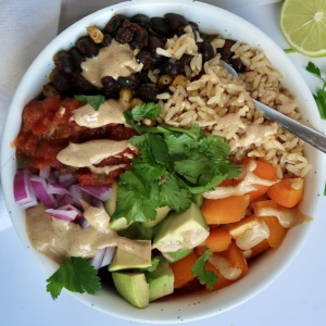 White bowl with spiced black beans and veggies inside as well as brown rice, salsa, and a creamy sauce on top