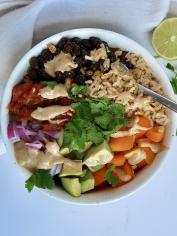 White bowl with spiced black beans and veggies inside as well as brown rice, salsa, and a creamy sauce on top
