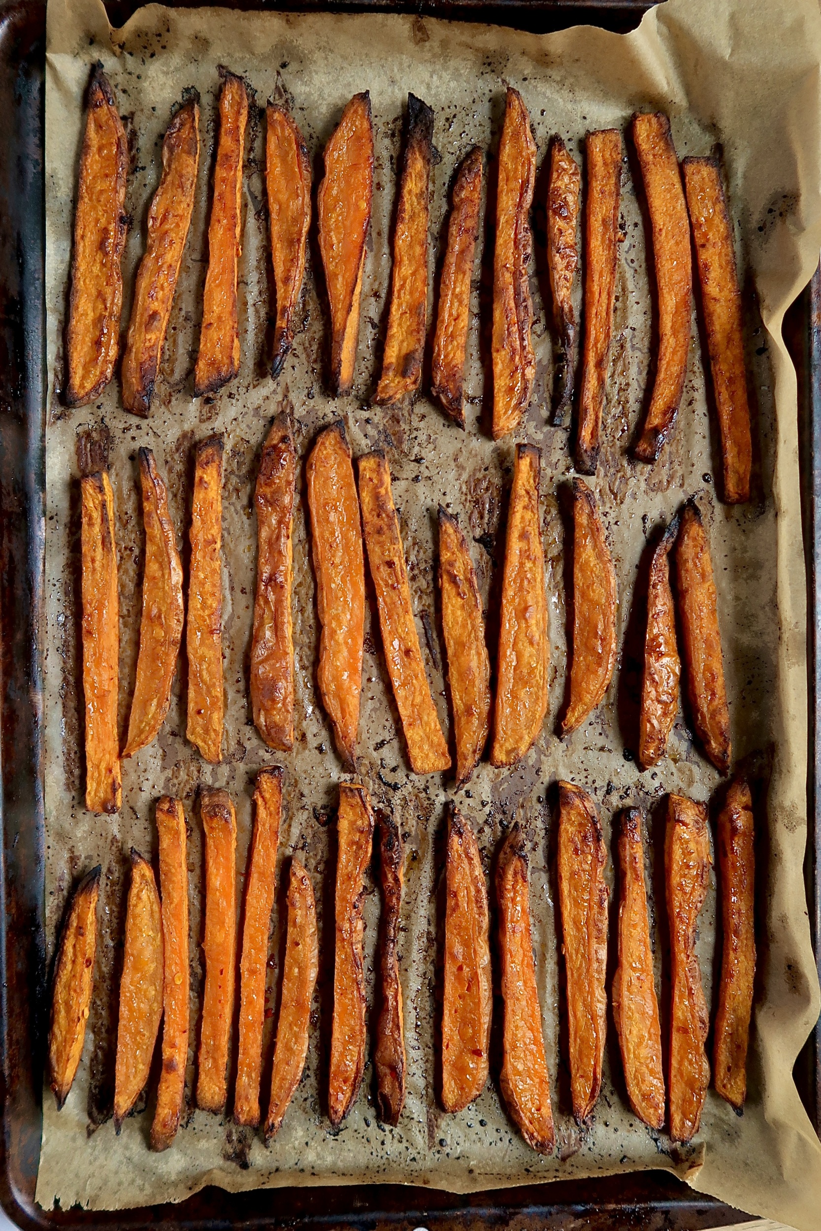 Sweet potato fries spaced out on a sheet pan that are crispy.