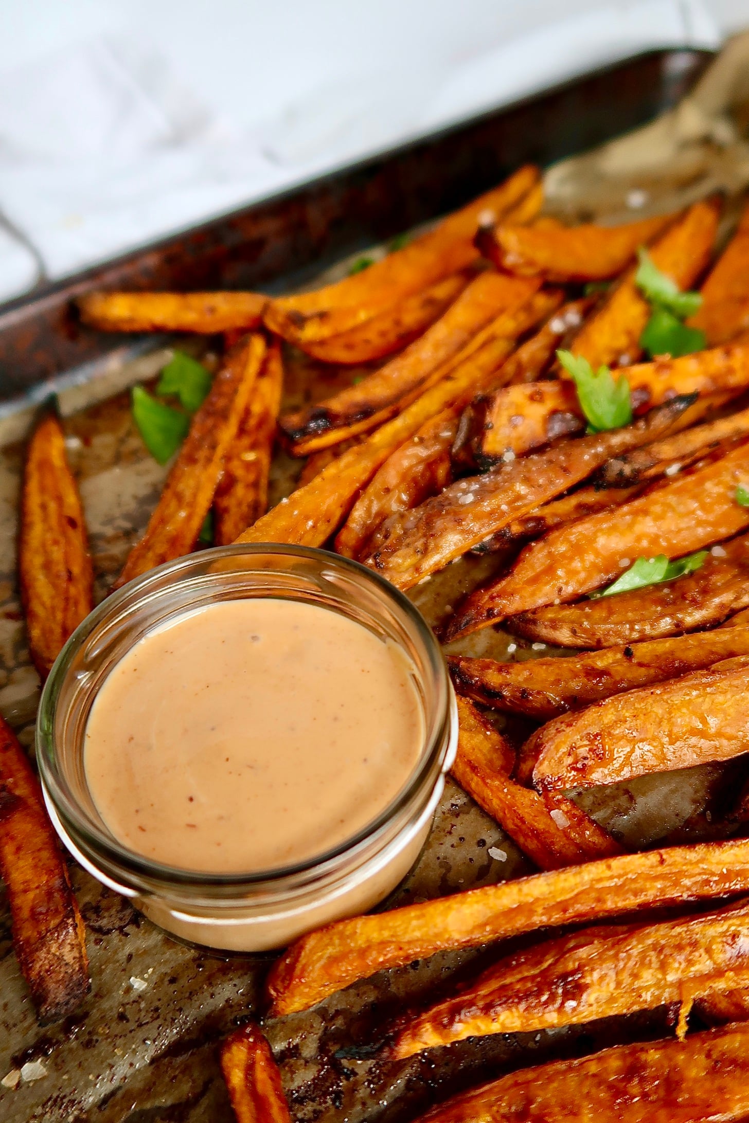Cooked sweet potato fries on a sheet pan and a creamy sauce in a small bowl on the side.