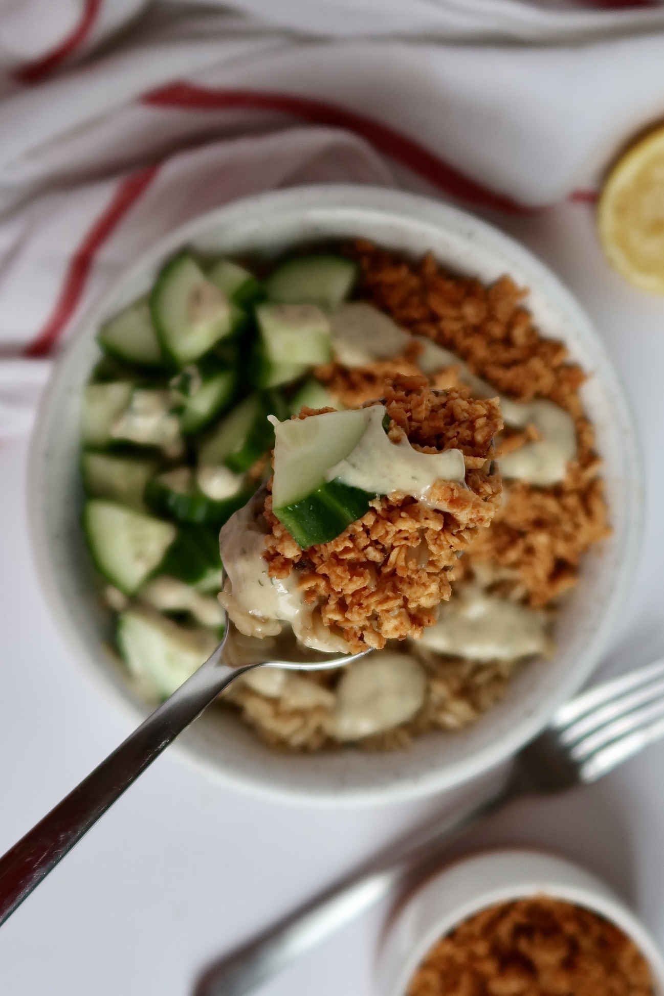 Shredded tofu in a bowl with cucumber and rice with tahini sauce drizzled on top and a spoon scooping some out.
