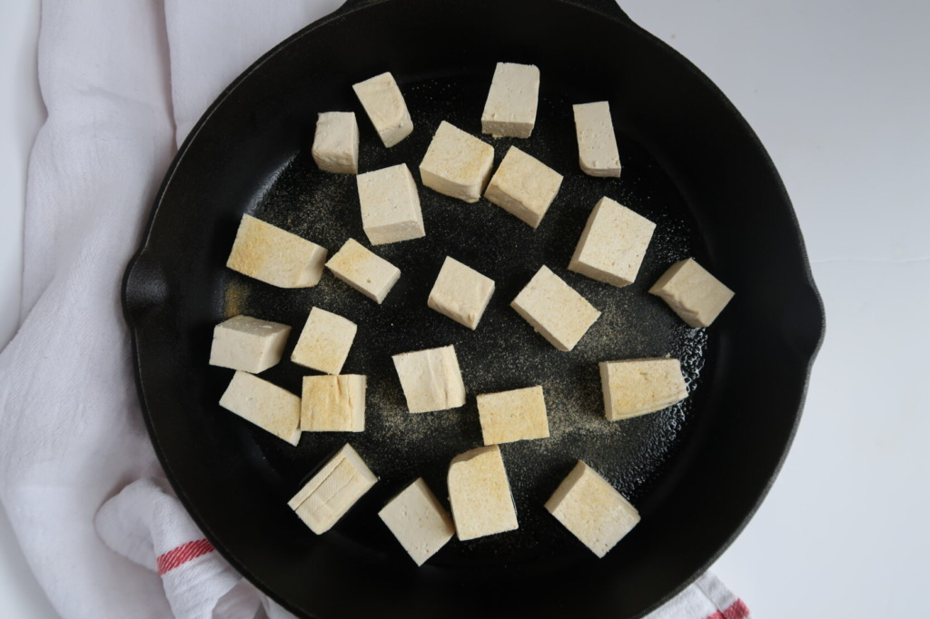 Cubed tofu in a cast iron pan with garlic powder on top.