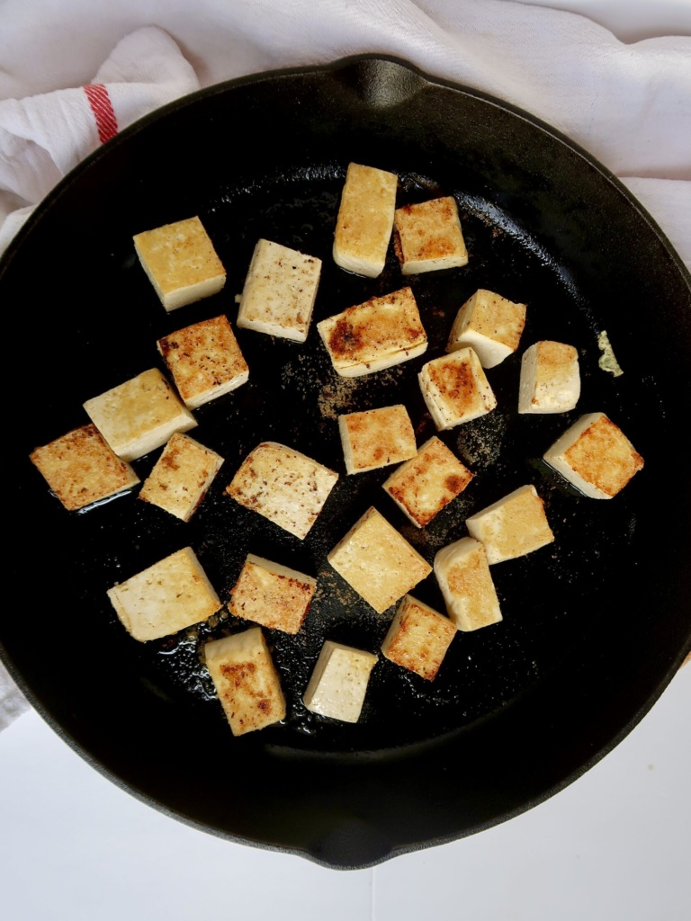 Golden brown cubed tofu in a cast iron pan with garlic powder on top.