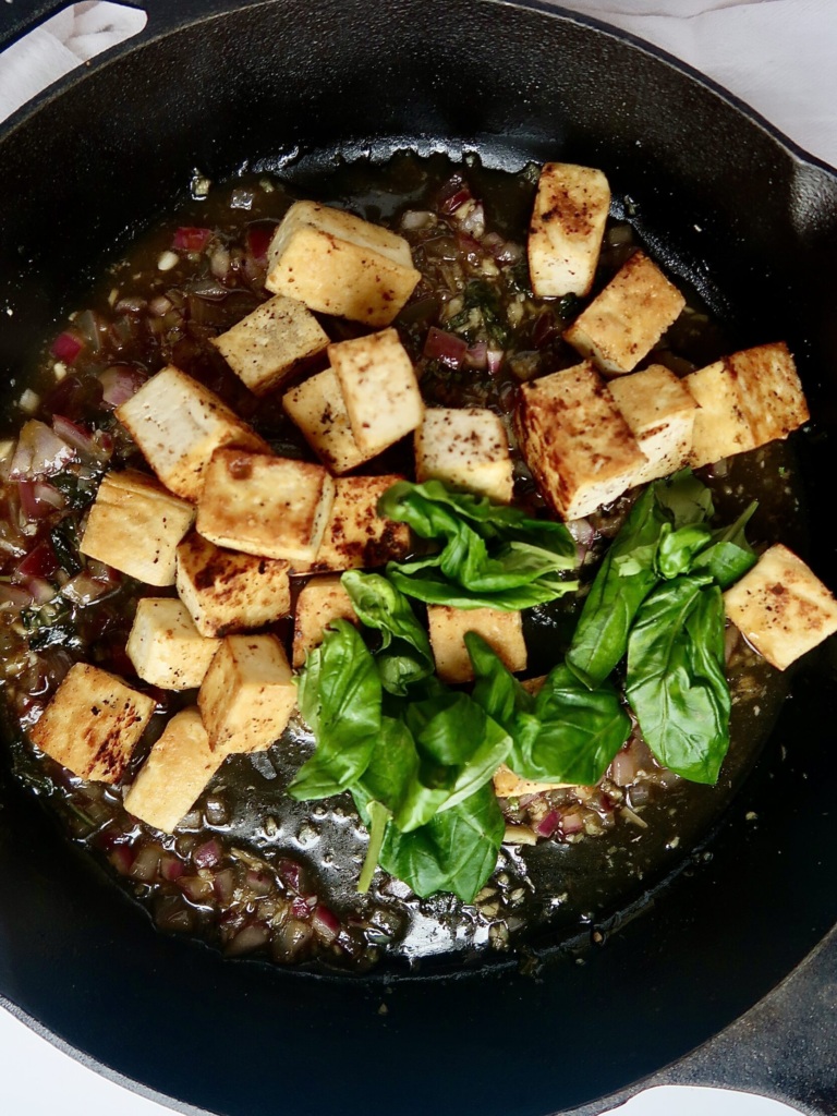 Golden brown tofu and wilted basil in a cast iron pan.