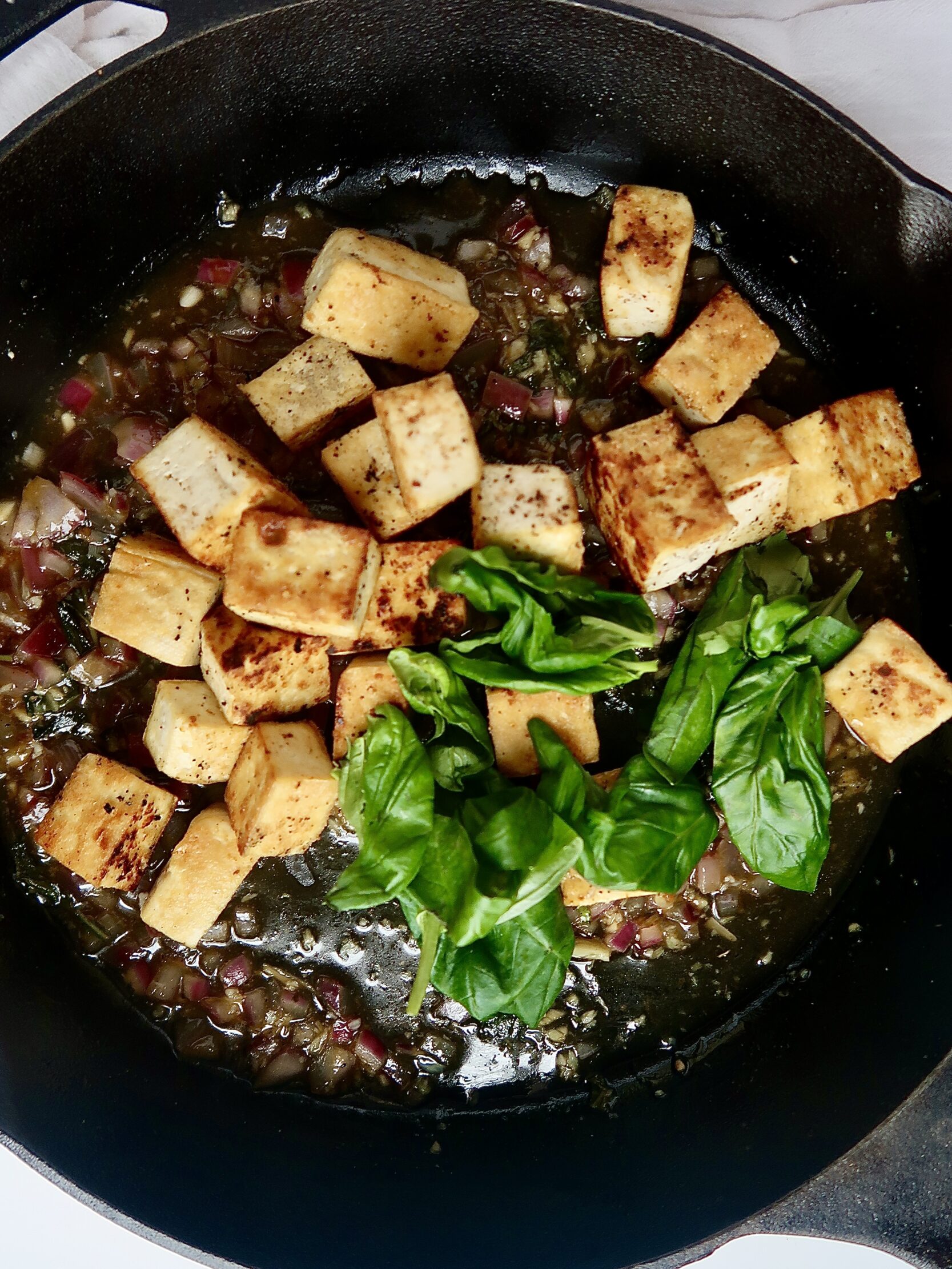 Golden brown tofu and wilted basil in a cast iron pan.