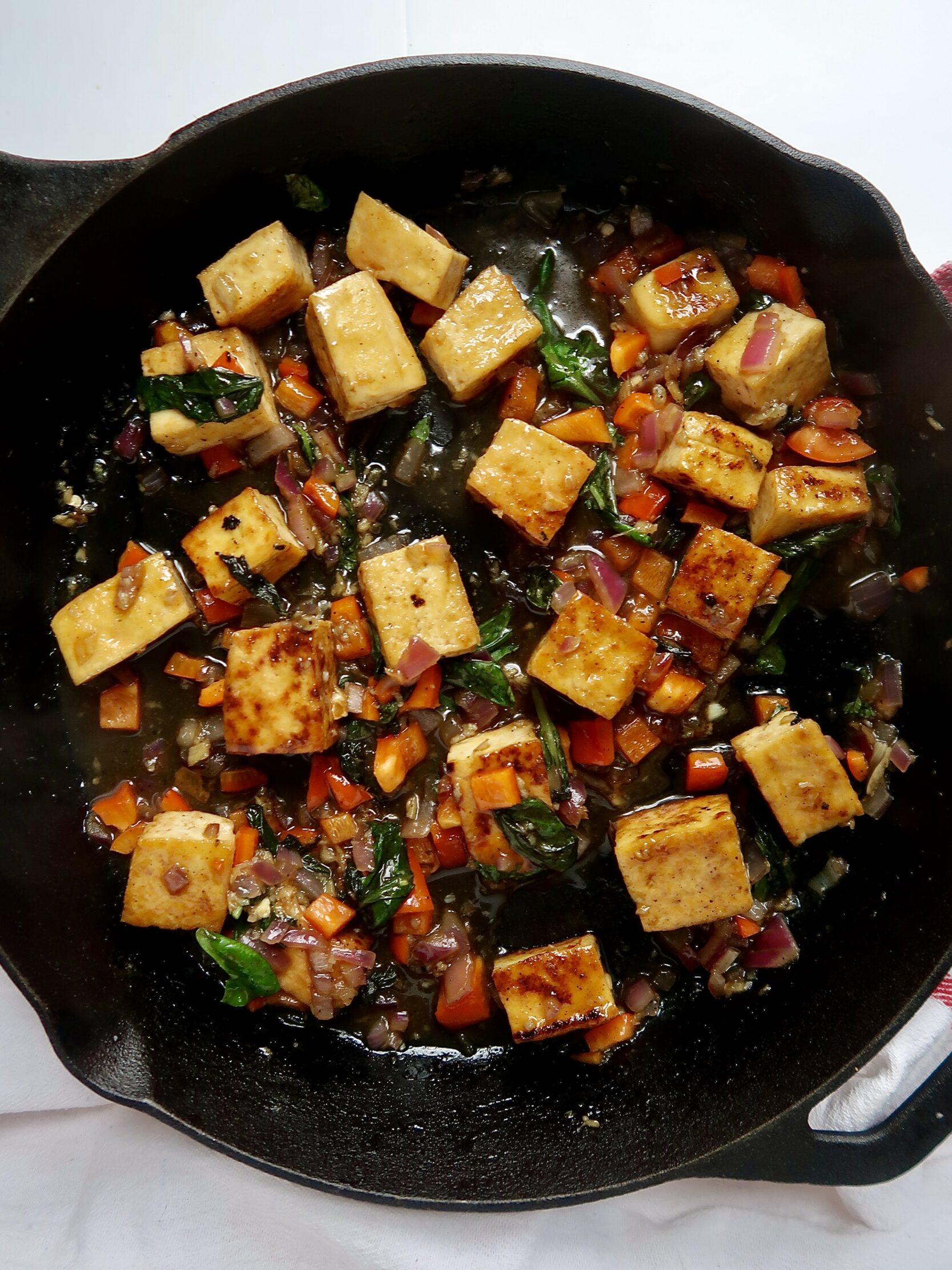 Golden brown tofu and chopped red pepper with basil in a cast iron pan.