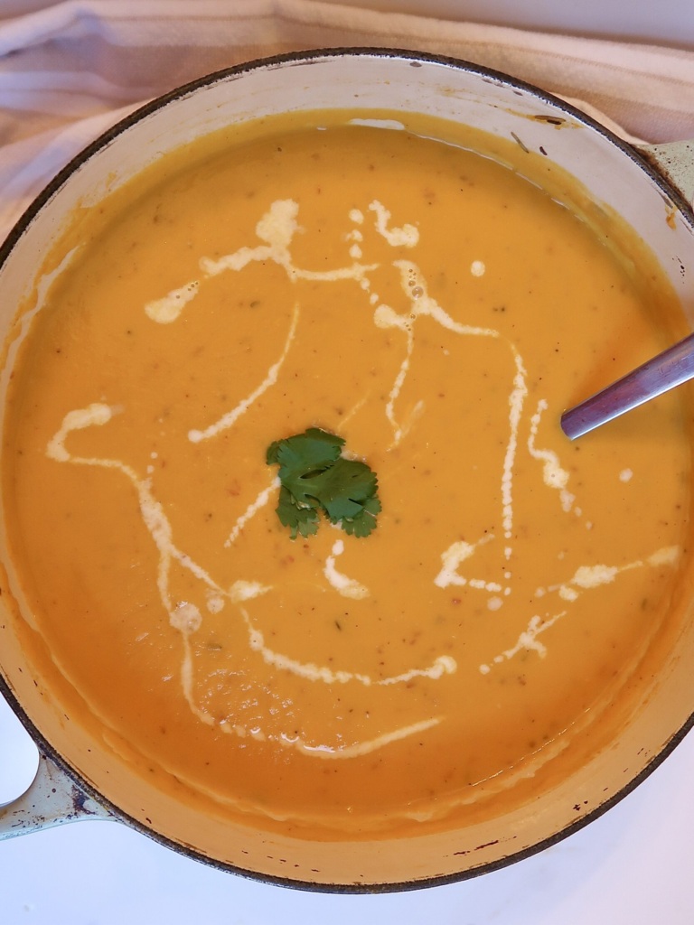 Blended sweet potato soup in a large pot with coconut milk drizzled on top.